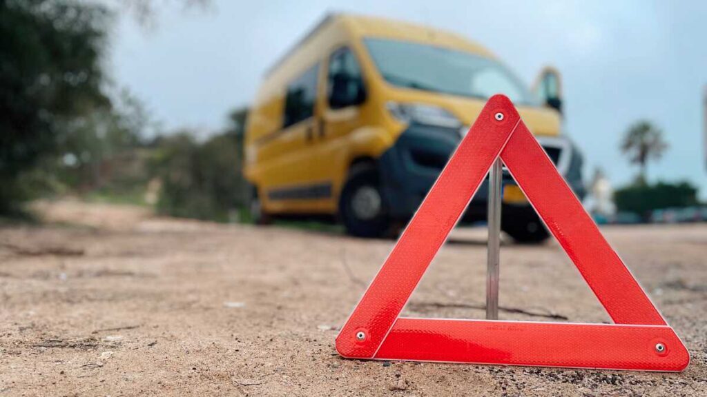 Red safety triangle in front of yellow van on a dirt road