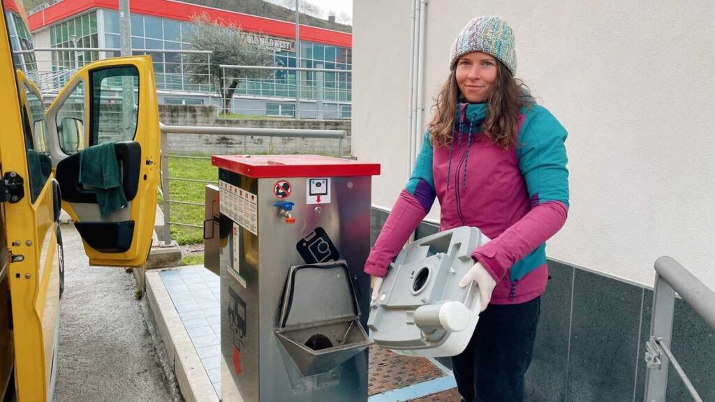 Woman in bright winter clothes with chemical toilet cassette in hands by a camper service point