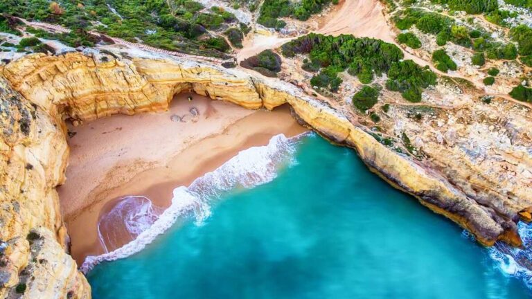 Drone shot of orange cliffs with white waves crashing over clear blue water