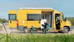 large yellow van parked on sand with picnic table and chairs beside