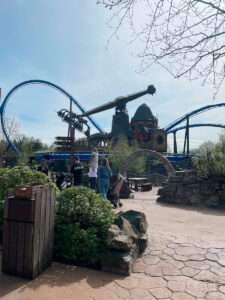 small green bushes with a stone pathway leading towards multiple large roller coasters