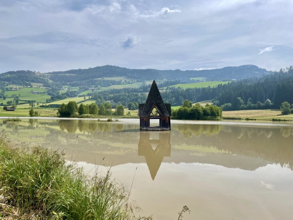 Rottenmannerbach tower has sunk into the lake, the top of which you can still see in the photo. All around you see green mountains and a brown lake